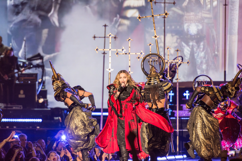 Madonna onstage singing in a red flowing cape with two Egyptian looking sarchophagi dancers. Taken live during her 